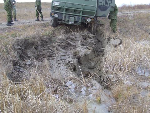 1990 Ford Bronco - A military truck is stuck in a muddy ditch, with two soldiers observing the situation.