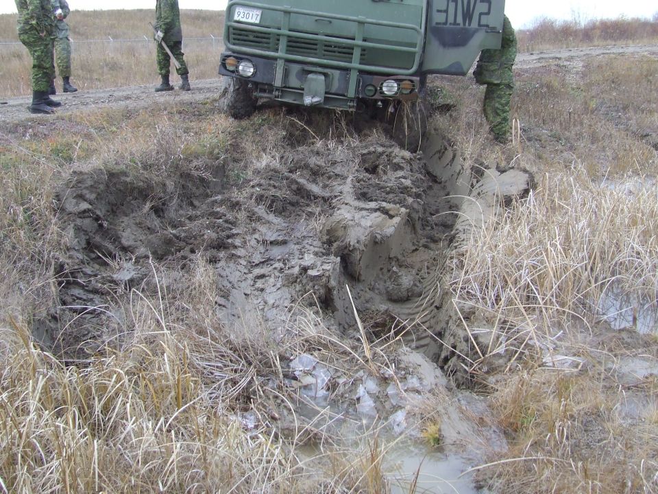 Military truck stuck in a deep mud pit with soldiers standing nearby