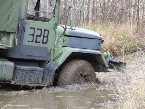 1990 Ford Bronco - A military truck is stuck in the mud on a recovery course, its front wheel deep in the mire.