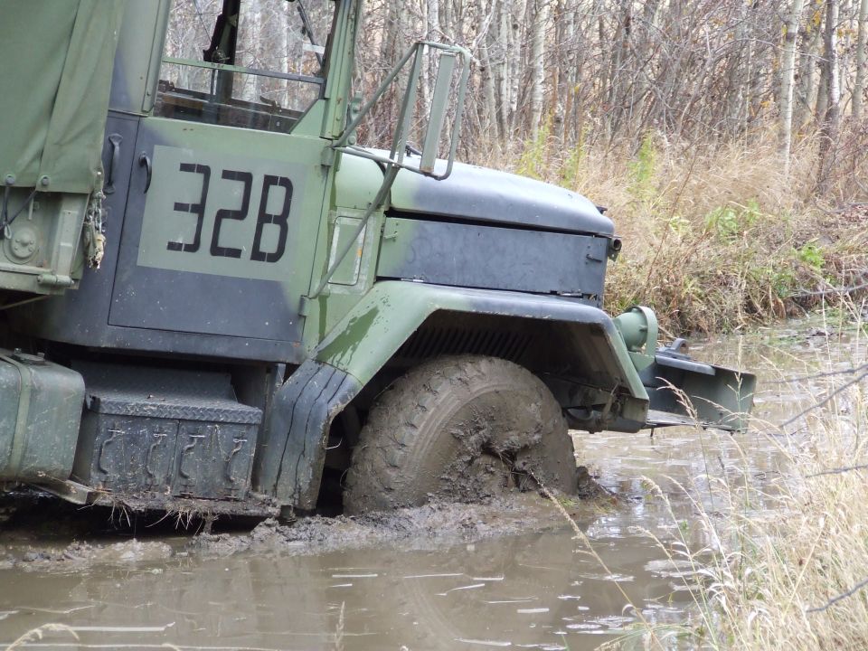 Military truck stuck in mud, front wheel submerged. Camouflage paint, number 32B visible on door