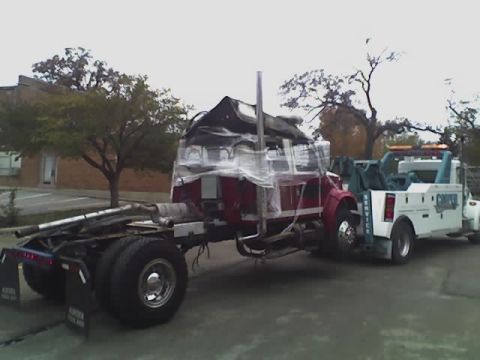 1992 Ford Bronco - A tow truck is transporting a damaged semi-truck cab that is covered in plastic wrap.