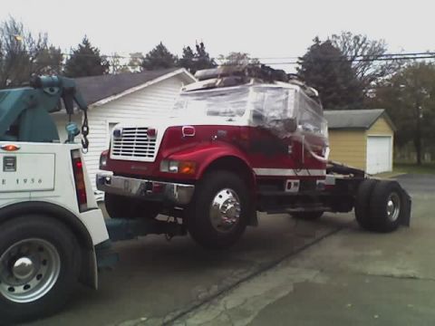 1992 Ford Bronco - A tow truck is hauling a red and white truck cab, which is covered in plastic wrap.