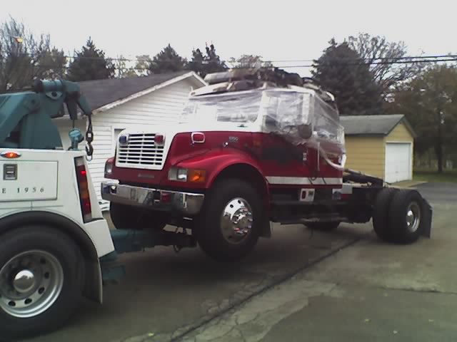 tow truck hauling a red and white truck cab covered in plastic wrap