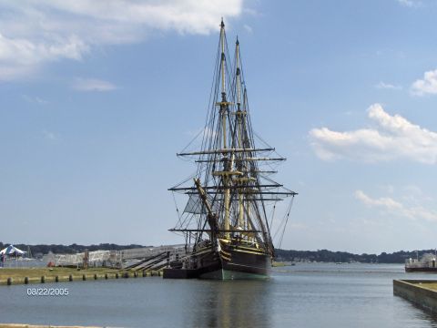 1996 Mercury Grand Marquis - A historic tall ship is moored at a dock on a sunny day, with a clear blue sky and scattered clouds overhead.