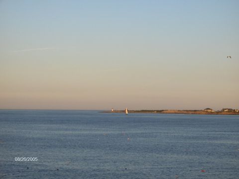 1996 Mercury Grand Marquis - A coastal scene at sunset features a sailboat navigating the calm waters near a distant lighthouse.