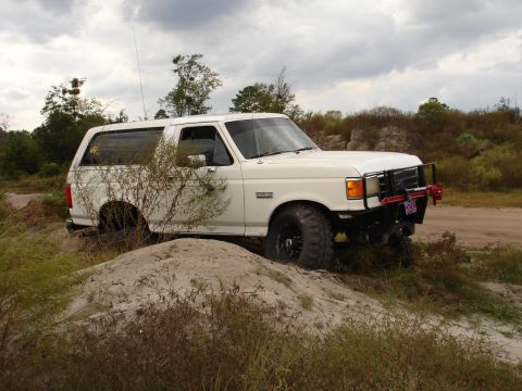 1989 Ford Bronco - White 1989 Ford Bronco navigating a sandy, off-road terrain under a cloudy sky.