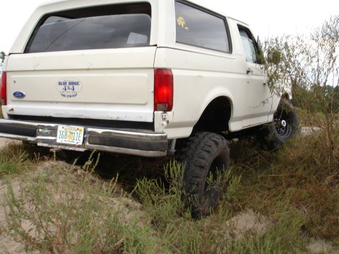 1989 Ford Bronco - This lifted Ford Bronco is navigating a sandy, overgrown trail.