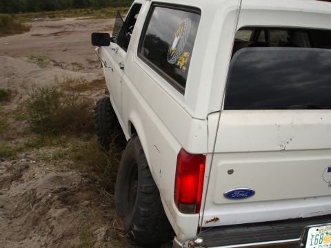 1989 Ford Bronco - White Ford Bronco with off-road tires parked on dirt.