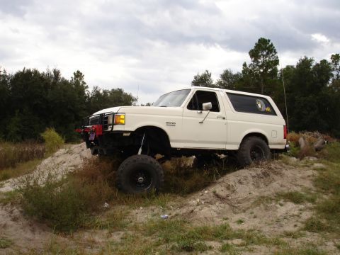 1989 Ford Bronco - White 1989 Ford Bronco with lifted suspension and off-road tires navigates a dirt hill.
