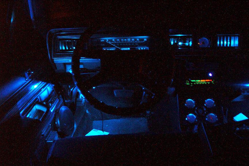 Car interior at night with blue underglow lighting on dashboard and floor. Steering wheel and radio visible