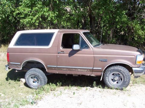 1995 Ford Bronco - A brown 1995 Ford Bronco is parked outdoors, displaying its side profile with off-road tires and a white top.