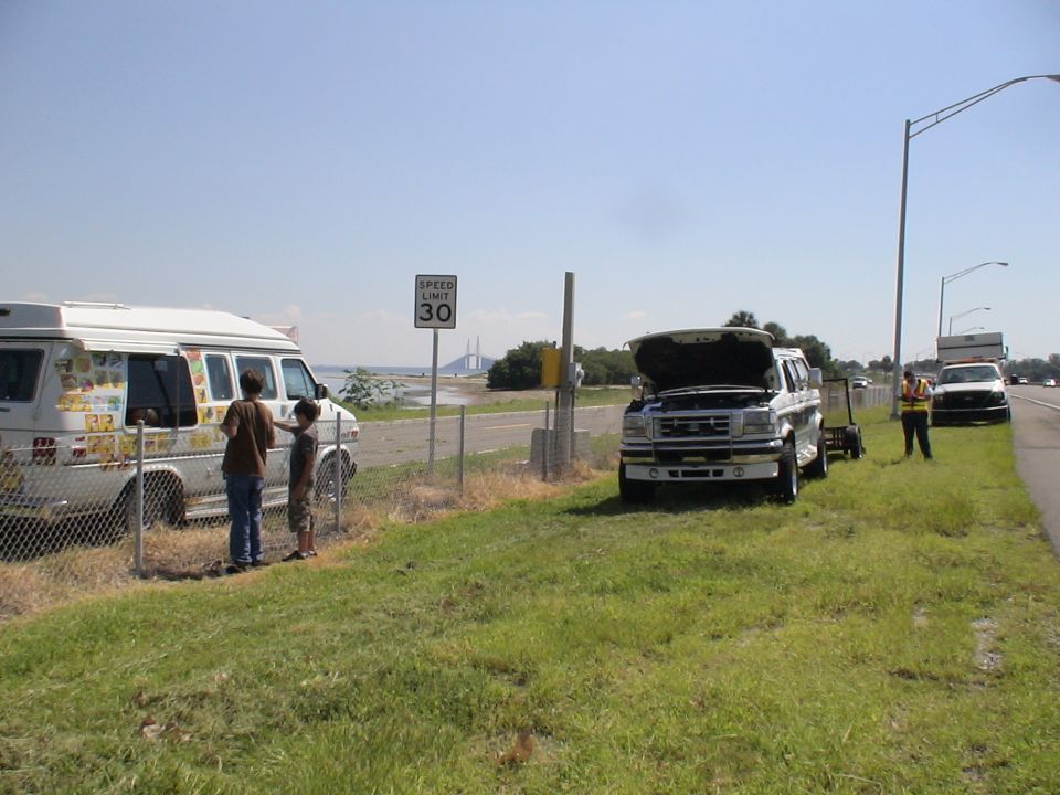 White Ford F-Series truck with hood open, parked on grassy shoulder next to an ice cream truck