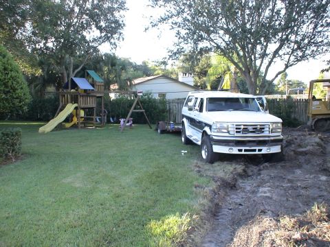 1993 Ford C-350 (Centurion Conversions) - White Ford Bronco SUV in a backyard with a playset and construction equipment nearby.