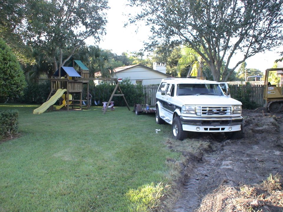 White Ford Bronco SUV parked on muddy ground next to a backyard playset