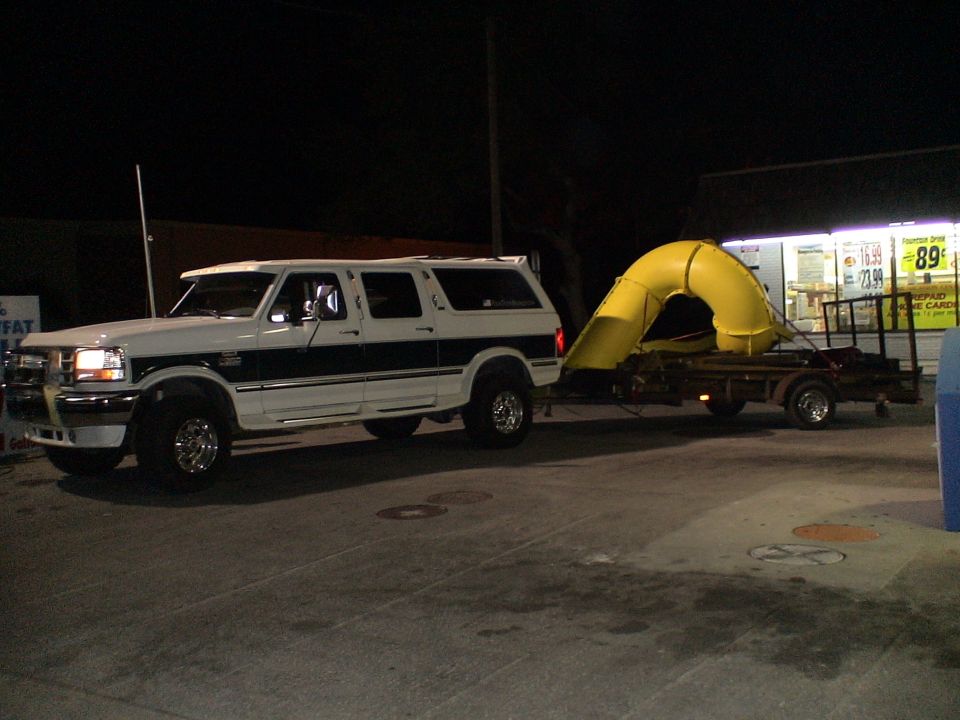 White and dark green SUV towing a yellow slide on a trailer at night