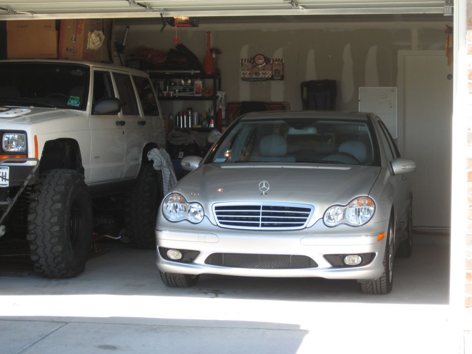 Silver Mercedes-Benz sedan front view in a garage next to a lifted Jeep