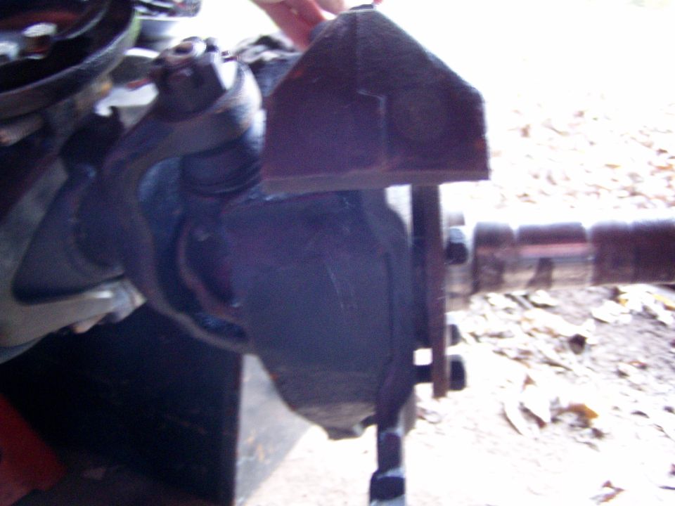 Close-up of a dark-colored suspension component with bolts and a metal shaft extending to the right