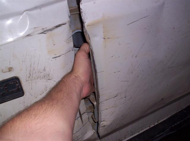 Damaged white vehicle door gap with a hand reaching into it