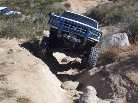 1995 Ford Bronco - A modified Ford Bronco tackles an off-road trail with large tires and a reinforced bumper.