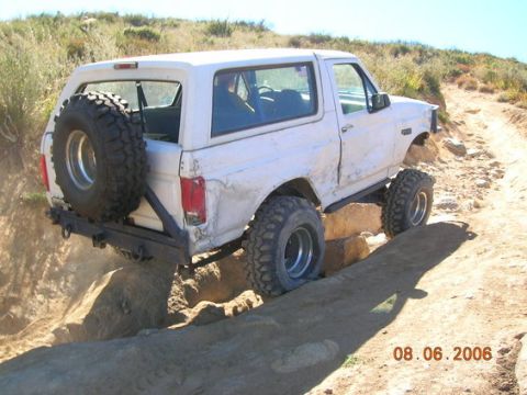 1995 Ford Bronco - A white Ford Bronco is shown traversing a challenging off-road path with large rocks.