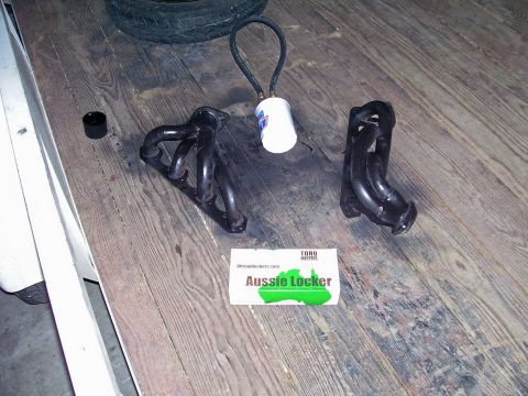 1991 Ford Bronco - Exhaust headers and a tire are laid out on a wooden floor, with a business card for Aussie Locker.