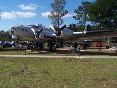 1973 Ford Ranchero - A B-17 Flying Fortress airplane is parked on grass with several cars visible in the background.