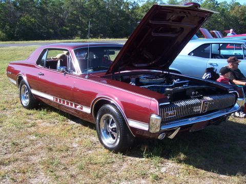 1973 Ford Ranchero - A red Mercury Cougar is displayed with its hood open at an outdoor car show.