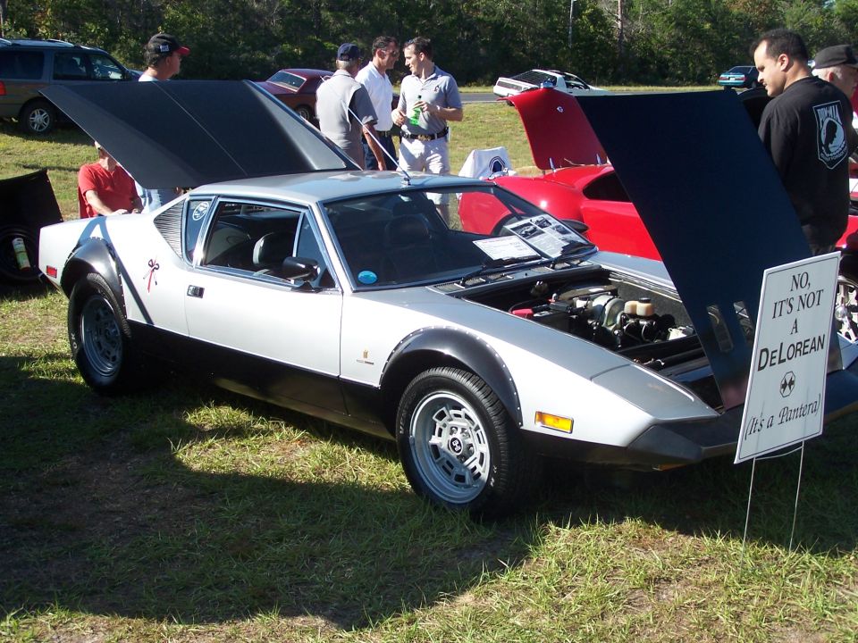 Silver De Tomaso Pantera with hood open, sign says 'NO. IT'S NOT A DELOREAN (It's a Pantera!)'