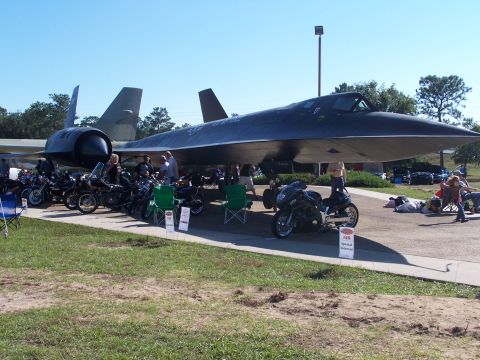 1973 Ford Ranchero - An SR-71 Blackbird aircraft is the centerpiece of this outdoor event, surrounded by a collection of motorcycles.
