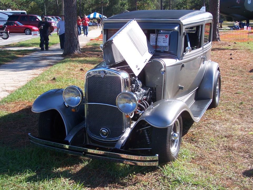 Gray 1930s sedan hot rod with hood open, showing engine. Chrome grille and bumper