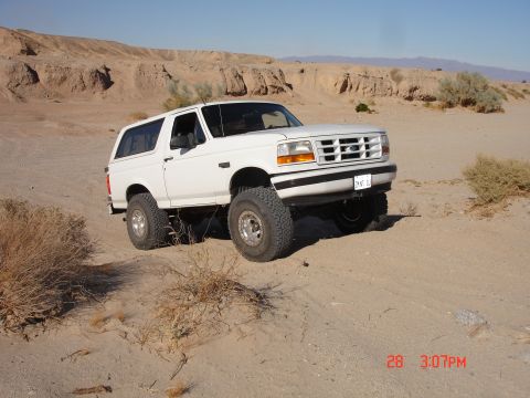1996 Ford Bronco - A white Ford Bronco is shown in a desert landscape with mountains in the background.