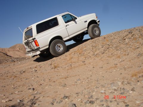 1996 Ford Bronco - A white SUV navigates a steep, rocky incline under a clear blue sky.