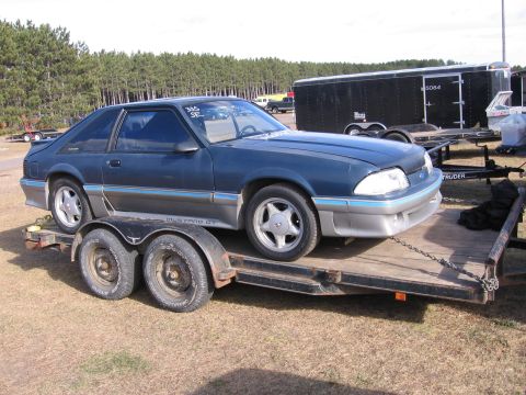 1989 Ford Mustang - A dark blue coupe, identified as a Mustang GT, is loaded onto a trailer.