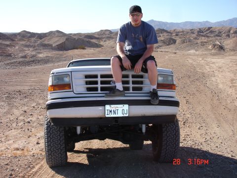 1996 Ford Bronco - A man sits atop the grille of a lifted white Ford F-150 truck in a desert landscape.