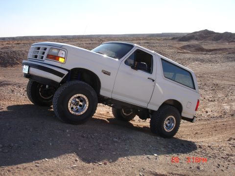 1996 Ford Bronco - This lifted 1996 Ford Bronco navigates a rocky, off-road terrain under a clear blue sky.