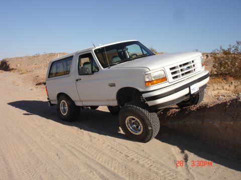 1996 Ford Bronco - A white 1996 Ford Bronco is shown off-road on a sunny day.