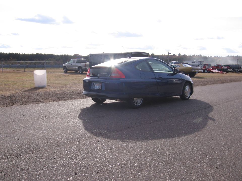 blue coupe on asphalt track, truck and trailers in background