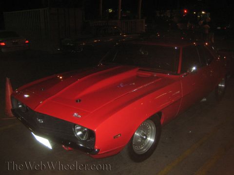 1968 Ford Mustang - A red muscle car is parked at night, showing its front quarter view with custom wheels and a prominent hood scoop.