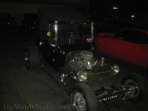 1968 Ford Mustang - A black hot rod with a prominent engine and chrome exhaust is parked next to a red car.