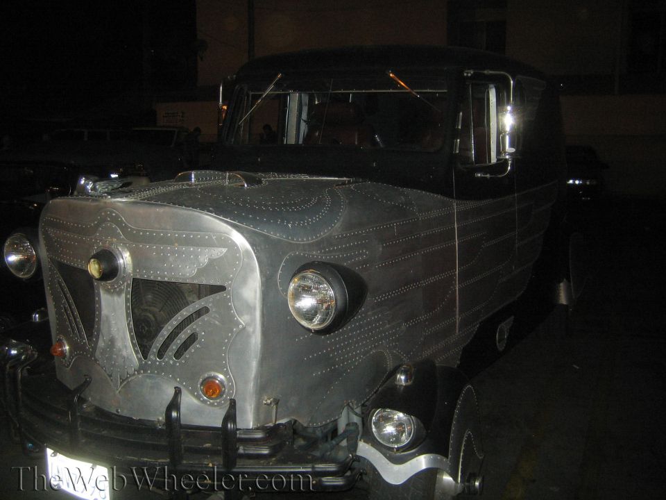 Custom riveted vehicle with a black top and silver body, parked at night