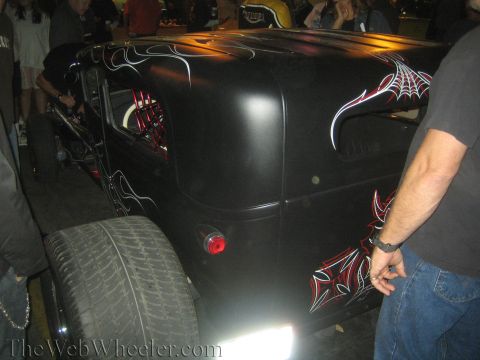 1968 Ford Mustang - A custom black hot rod with flame and spiderweb graphics is viewed from the rear, with people gathered around.