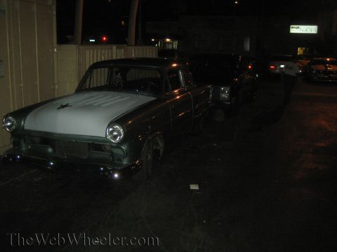 1968 Ford Mustang - A dark green sedan with a light grey hood is parked at night, with other vehicles visible in the background.