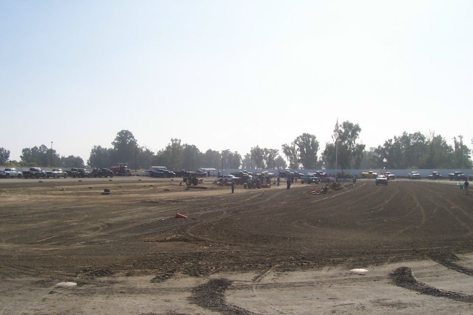 Dirt lot with numerous cars and trucks parked in the background under a hazy sky