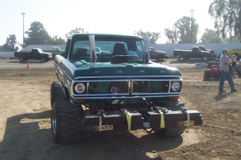 1994 Ford F-150 - A heavily modified green Ford pickup truck with large tires and dual exhaust stacks sits in a dirt lot.