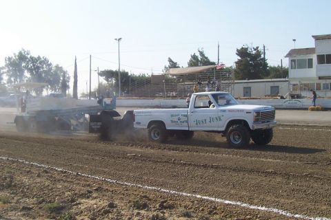 1994 Ford F-150 - A modified pickup truck competes in a pulling event, kicking up dust as it drags a heavy load.