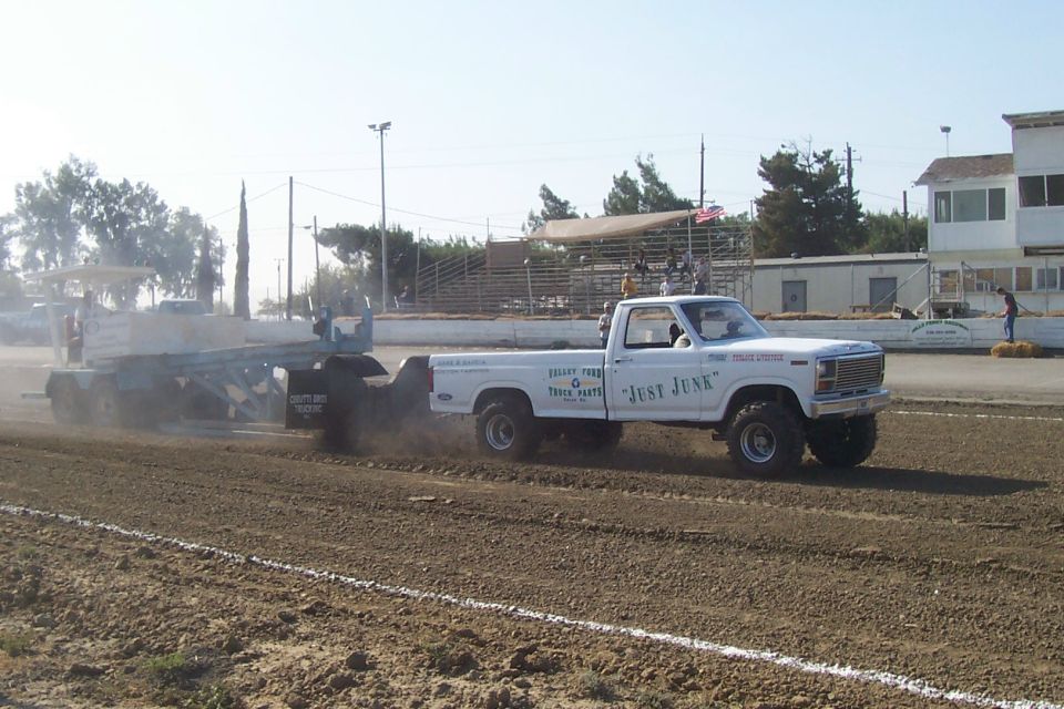 White pickup truck with "Just Junk" on the door, pulling a trailer in a dirt arena