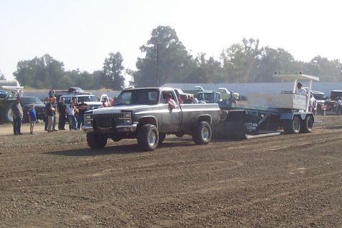 1994 Ford F-150 - A lifted pickup truck pulls a trailer through a dusty arena, with spectators gathered in the background.