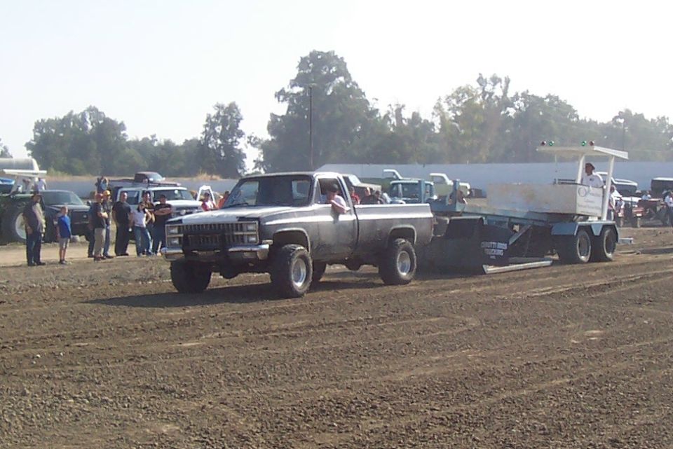 Gray pickup truck with lifted suspension towing a trailer in a dirt field