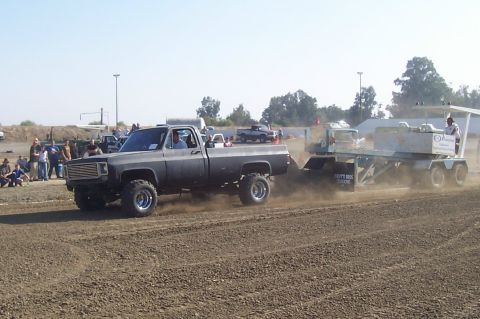 1994 Ford F-150 - A modified pickup truck competes in a pull event, kicking up dust as it drags a weighted sled across the track.