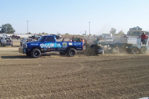 1994 Ford F-150 - A blue pickup truck competes in a pull event, dragging a weighted sled across a dirt track.